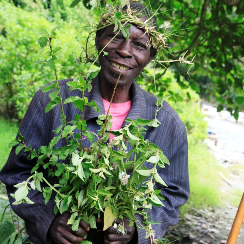 a man smiling holding a plant and wearing a leaf headdress at a ceremony