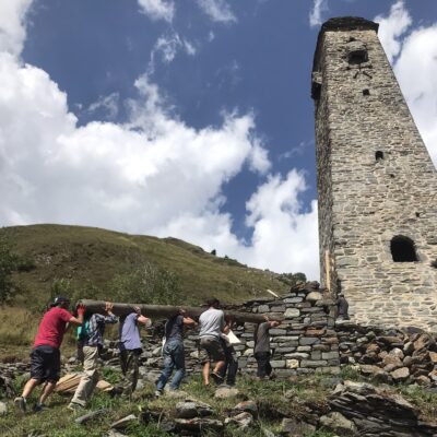 volunteers walks to a tall stone medieval tower in a mountainous landscape award