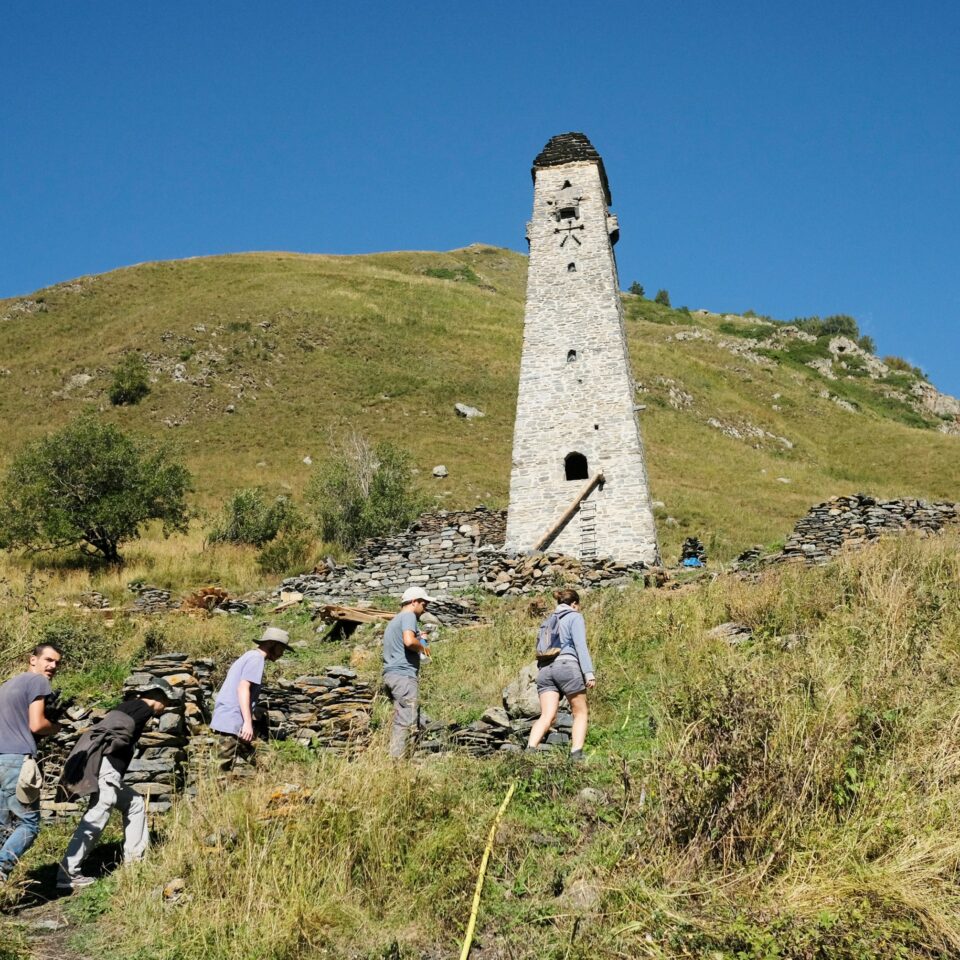 a tall stone tower in a mountain landscape with people in the foreground