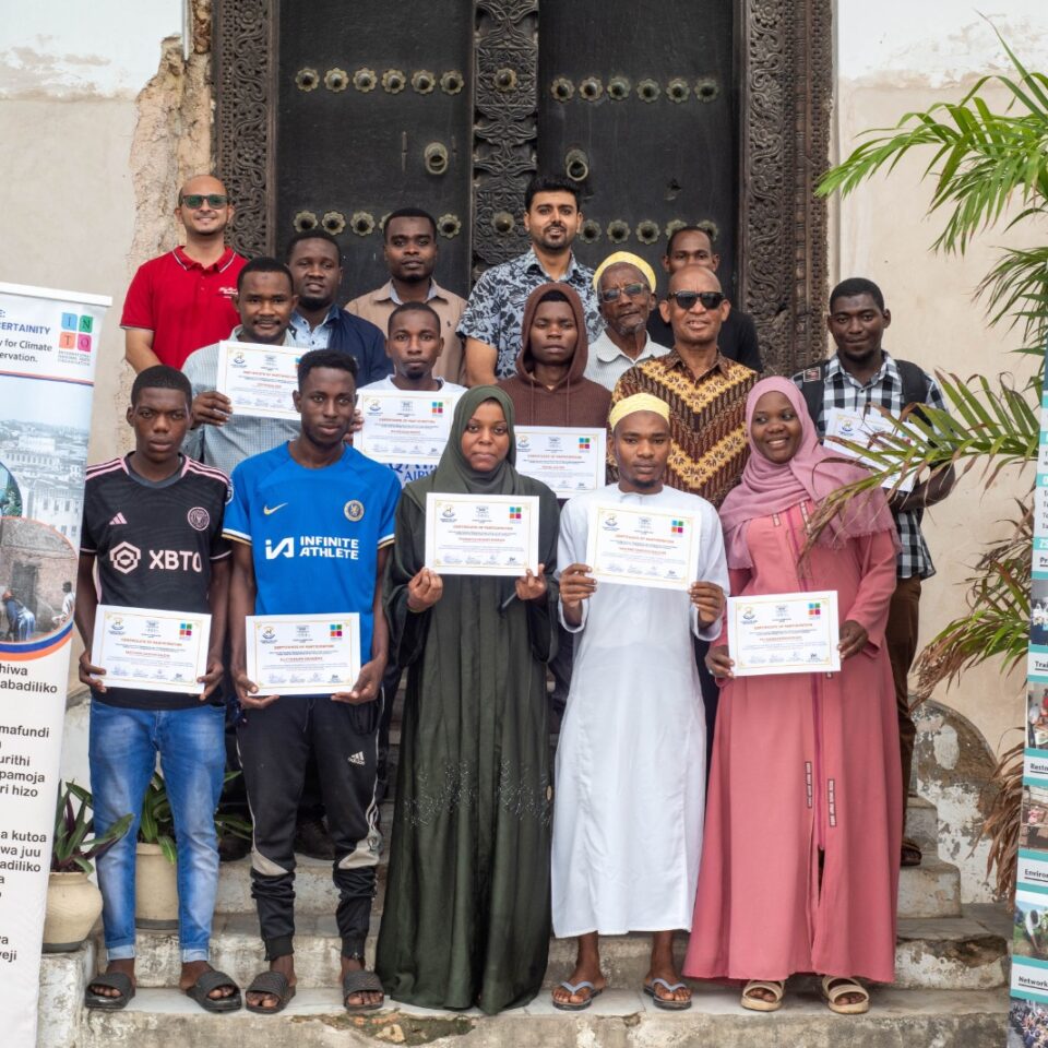 a group of people holding certificates in front of the door of the Old Customs House in Zanzibar