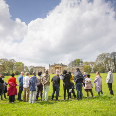 a group of people standing on green grass looking towards a grand building