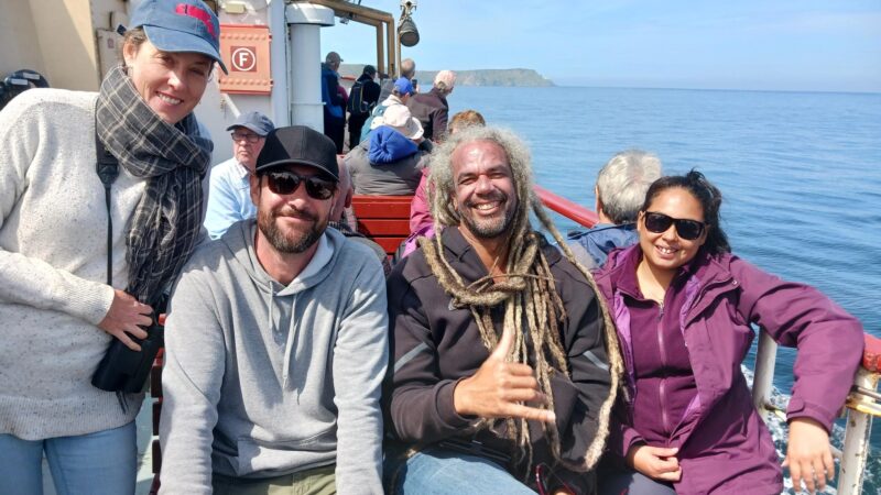 four people smiling at the camera, sitting on a boat with blue skies
