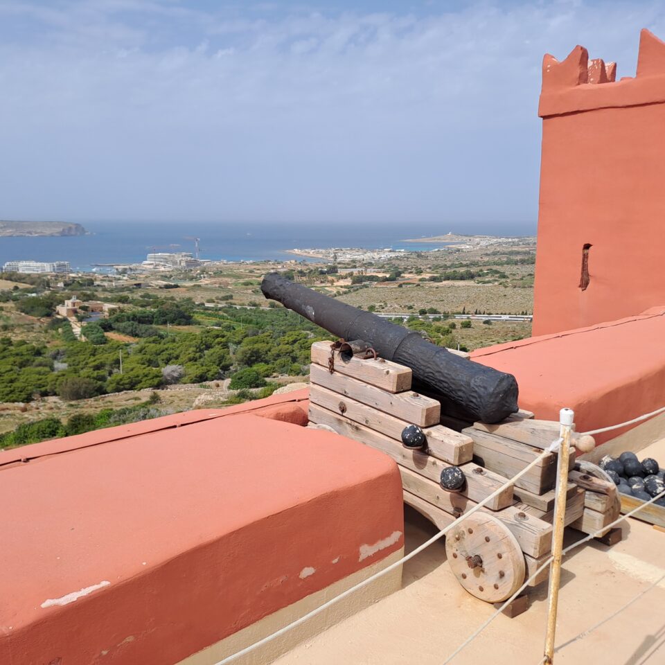 a photo showing a view at the Red Tower in Malta, with a cannon positioned on the wall surrounding the tower