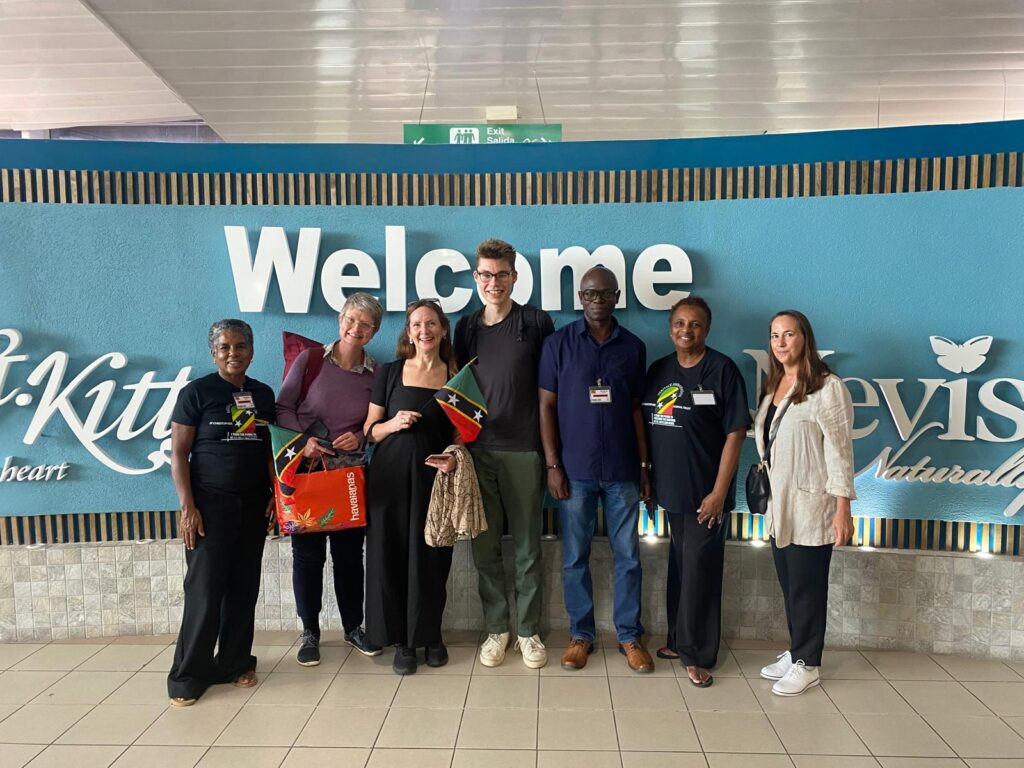 a group of people standing in front of a sign saying welcome to st kitts and nevis, smiling at the camera - blog title whose past