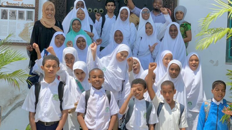 a large group of children in Zanzibar wearing white school uniforms and smiling at the camera