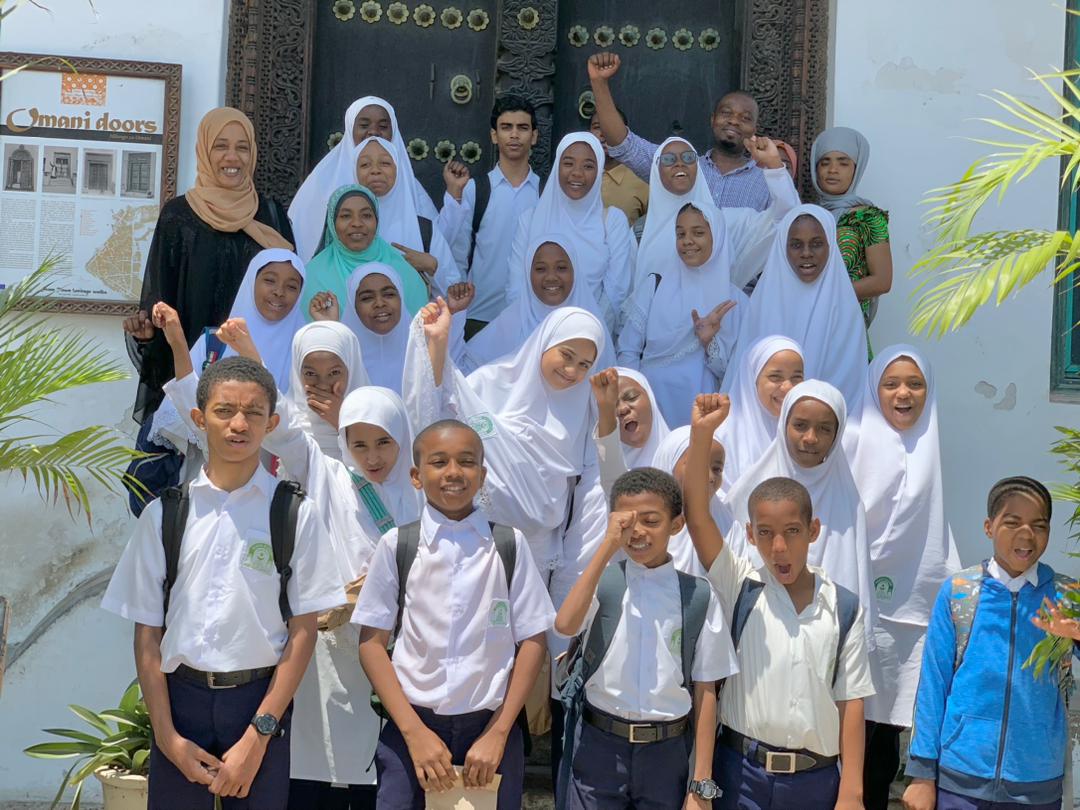 a large group of children in Zanzibar wearing white school uniforms and smiling at the camera