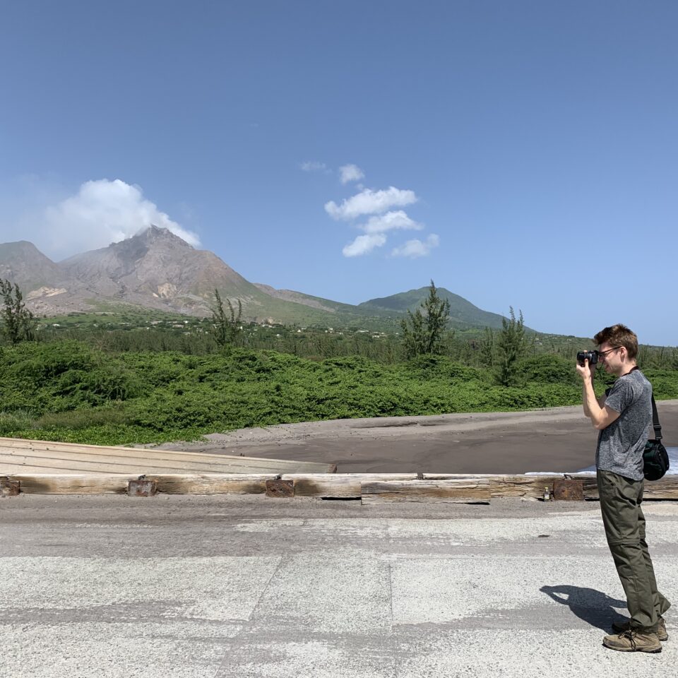 a person taking a photograph in an open landscape in St Kitts, with tropical mountains and blue skies for the blog whose past