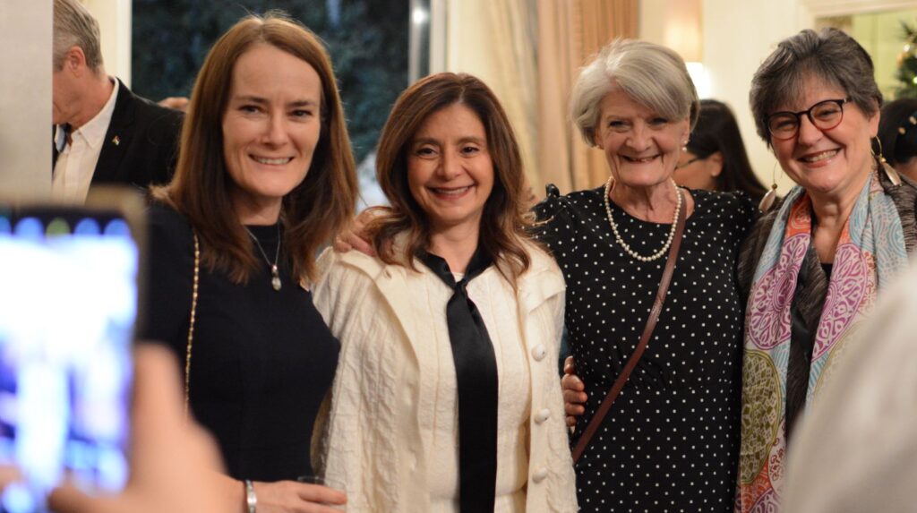 four women smiling at the camera with a phone camera in the foreground