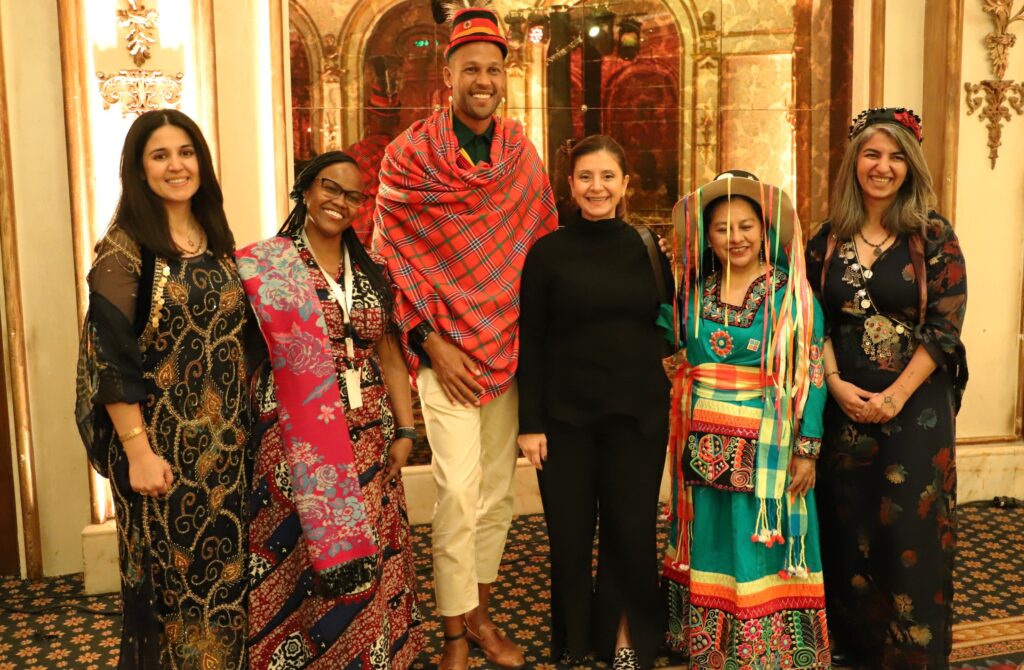 a group of 6 people in colourful traditional dress from India, Palestine, Bolivia and Uganda