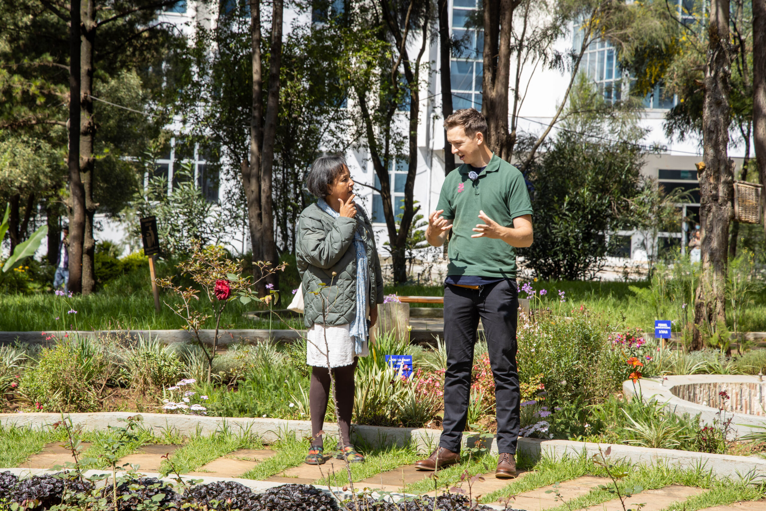 a man and a woman conversing in a garden - the man is gesturing with his hands