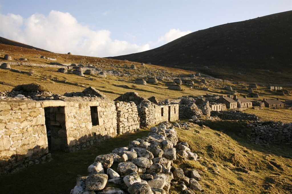 single storey stone buildings without rooves in a grassy and rocky landscape