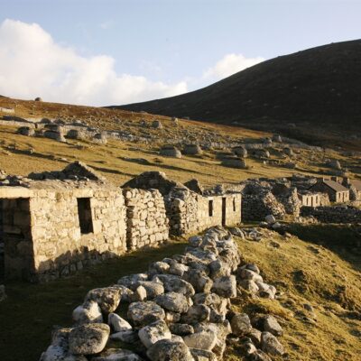 single storey stone buildings without rooves in a grassy and rocky landscape